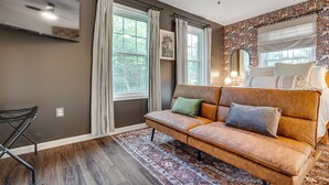 A living room with a brown leather sofa, a patterned rug, and a large window with curtains.