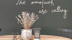 A table with a vase of dried flowers, a QR code sign, and a wall with a motivational quote.