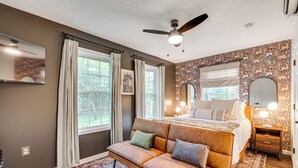 A bedroom with a large bed, a sofa, a ceiling fan, and a patterned wall.