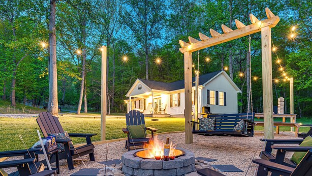 An outdoor patio area with Adirondack chairs, a fire pit, and a pergola with string lights.