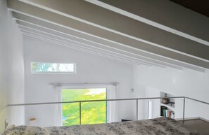 A bedroom with a large window, a bed with a patterned bedspread, a small balcony, and a view of a green landscape.