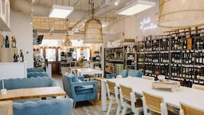 Et restaurantinteriør med blåt sæde, hvide borde og et vinskab i baggrunden.