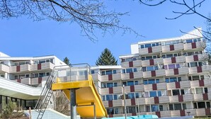 Un edificio moderno con varios balcones, un tobogán amarillo y una zona de piscina.