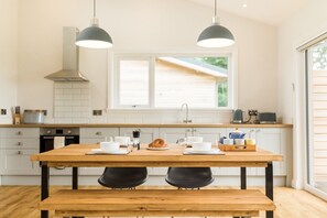 Een moderne keuken met een houten tafel, twee zwarte stoelen en hanglampen.