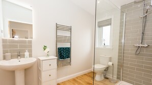 Een badkamer met een witte wastafel, een spiegel, een handdoekrek, een toilet en een douche.