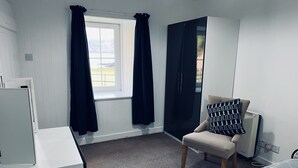 A room with a bed, a chair with a patterned pillow, a window with curtains, and a radiator.