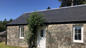 A stone house with a dark roof, a white door, and two windows.