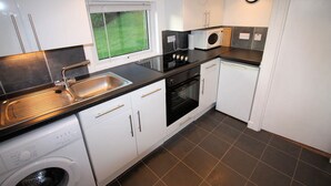 A modern kitchen with white cabinets, a black countertop, a built-in oven, a microwave, and a washing machine.
