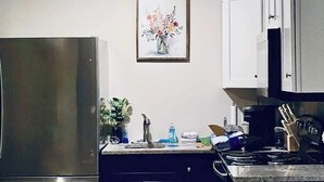 A compact kitchen with a refrigerator, cabinets, a sink, and a coffee maker.