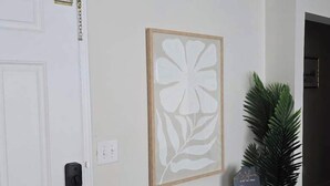 A hallway with a white door, a wooden bench, a framed artwork, and a potted plant.