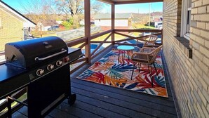 A covered outdoor area with a barbecue grill, a patterned rug, and outdoor furniture.