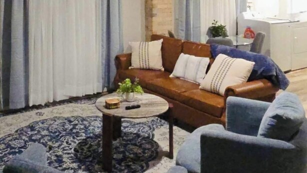 A living room with a brown sofa, two armchairs, a coffee table, and a clock on the wall.