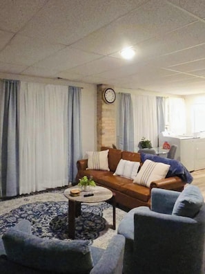 Ein Wohnzimmer mit braunem Sofa, zwei Sesseln, einem Couchtisch und einer Wanduhr.