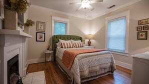 Un dormitorio con una cama, chimenea, ventilador de techo e imágenes enmarcadas en la pared.