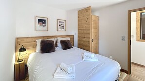A bedroom with a wooden headboard, two framed pictures on the wall, a wooden wardrobe, and two towels on the bed.