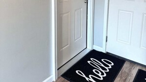 A hallway with two white doors, one with a number plate and a doormat with 'hello' written on it.