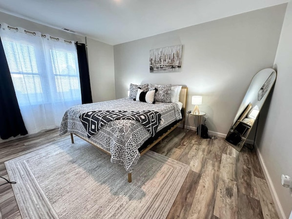 A bedroom with a bed, a bedside lamp, a mirror, and a window with curtains.