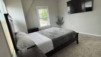 Ein Schlafzimmer mit einem Bett, einem Nachttisch, einem Deckenventilator, einem Fenster und einem an der Wand befestigten Fernseher.