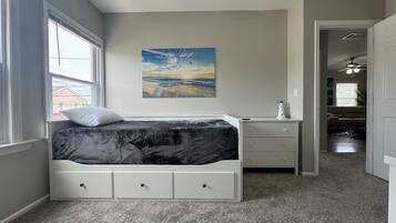 A bedroom with a bed, a nightstand, a painting, and a view of the living room.