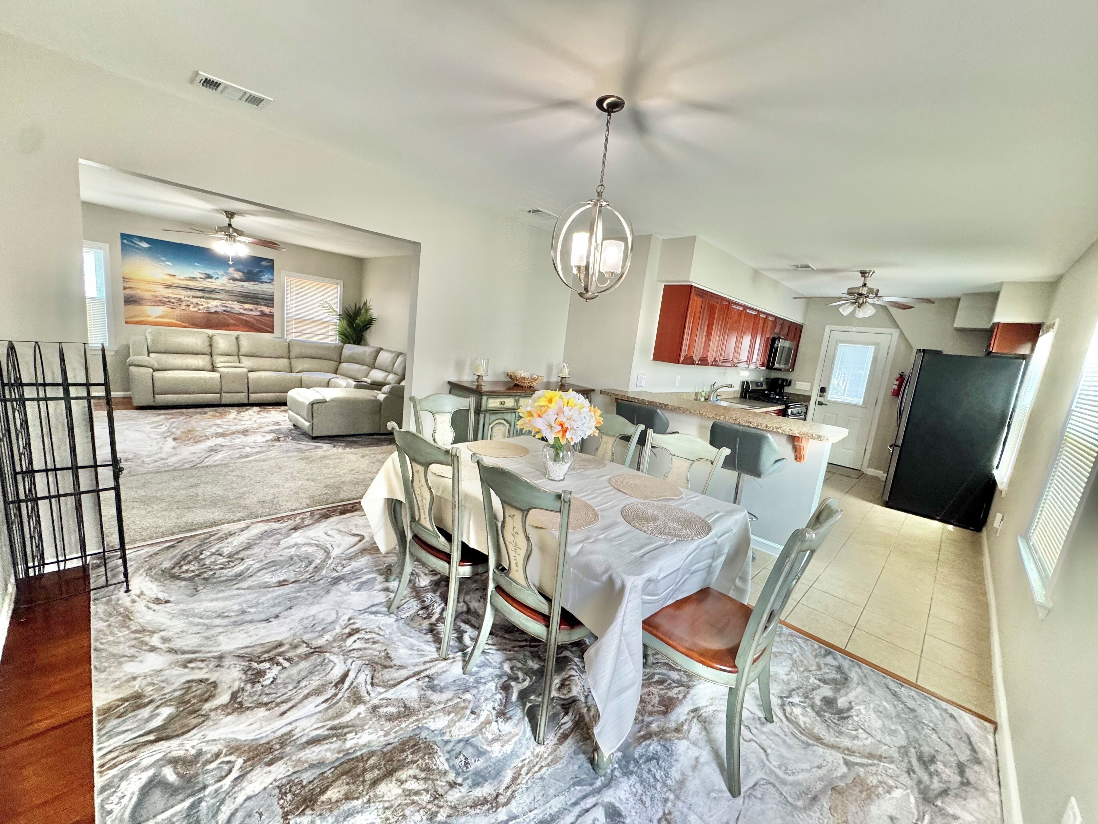A spacious living area with a dining table, chairs, a sofa, and a kitchen in the background.