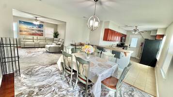 A spacious living area with a dining table, chairs, a sofa, and a kitchen in the background.
