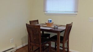 Un comedor con una mesa de madera y cuatro sillas, una ventana con persianas y un enchufe en la pared.
