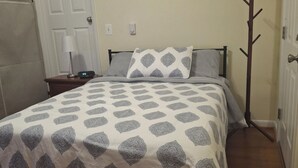 Un dormitorio con una cama, una mesita de noche, una lámpara, un perchero y una puerta.