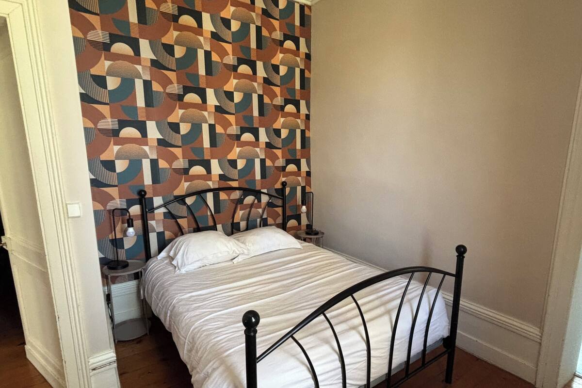 Une chambre à coucher avec un lit, un papier peint à motifs, une table de chevet et une lampe.