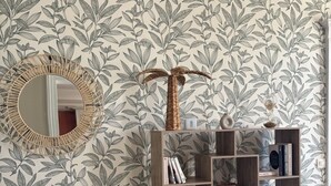 A room with a bookshelf filled with books, a mirror with a circular frame, and a wall with a leafy pattern.