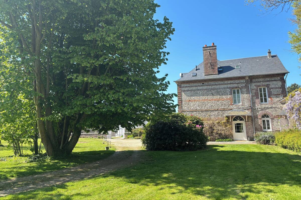 Un grand bâtiment en pierre, doté d’une cheminée en briques, entouré d’une pelouse bien entretenue et d’un grand arbre.