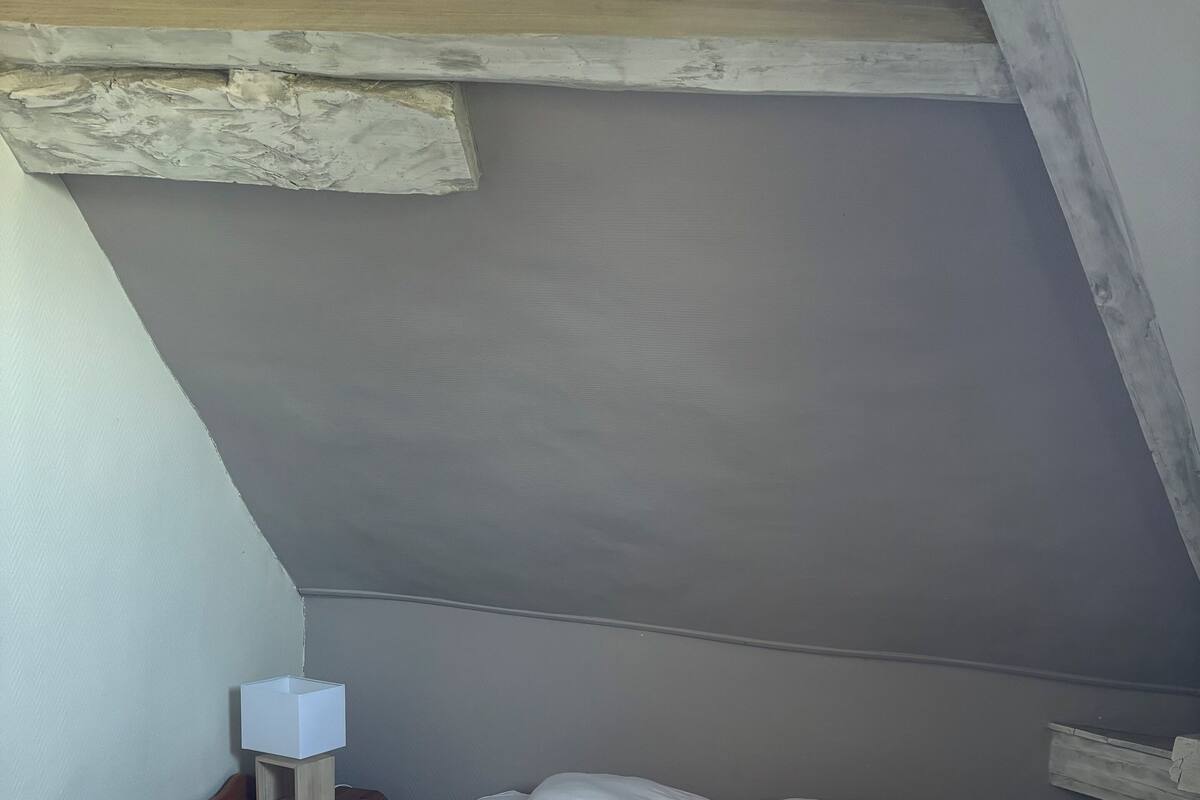 Une petite chambre avec un lit simple, un plafond en pente, une table de chevet avec une lampe et un radiateur.