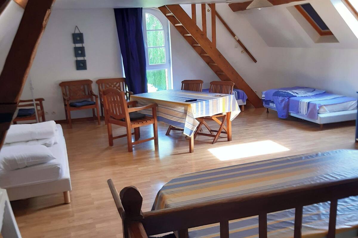Une chambre à coucher aménagée dans un espace mansardé, avec un plafond en pente, des meubles en bois, un lit, une table et une fenêtre.