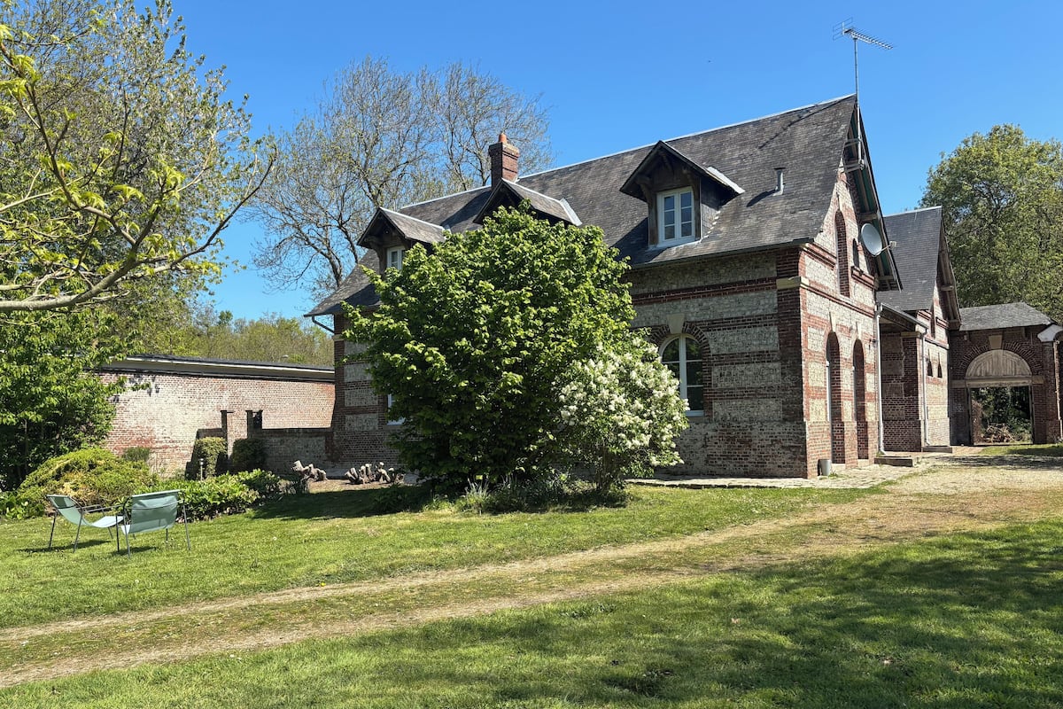 Un bâtiment historique à la façade en briques, doté de nombreuses cheminées et surmonté d’un grand arbre en premier plan.