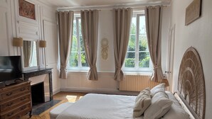 A bedroom with a bed, a TV, a dresser, and a window with curtains.