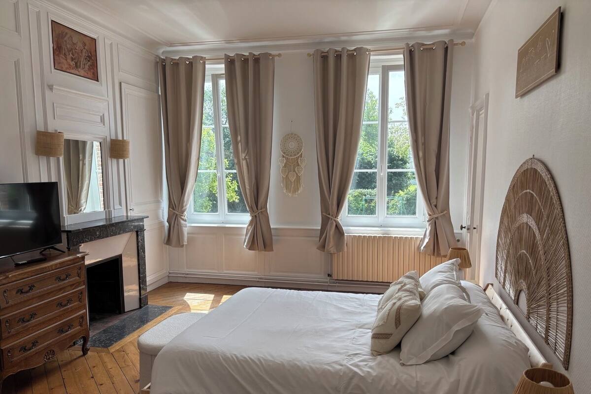 Une chambre à coucher avec un lit, une télévision, une commode et une fenêtre avec des rideaux.