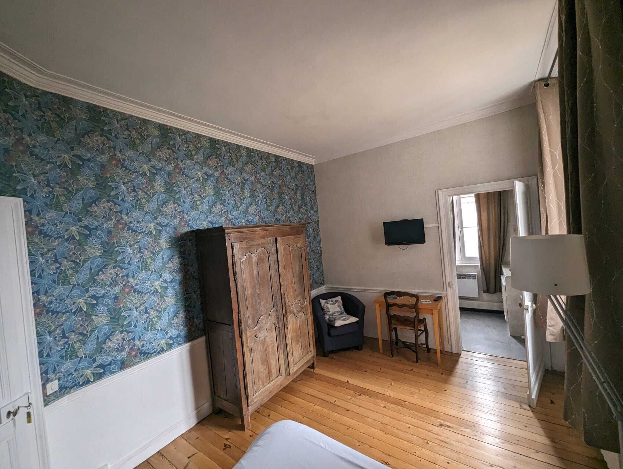 A room with wooden flooring, a wardrobe, a small table with a chair, and a television on the wall.