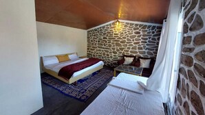 Ein Schlafzimmer mit Steinwand, einem Bett mit roter Decke, einem kleinen Tisch und einem Nachttisch.