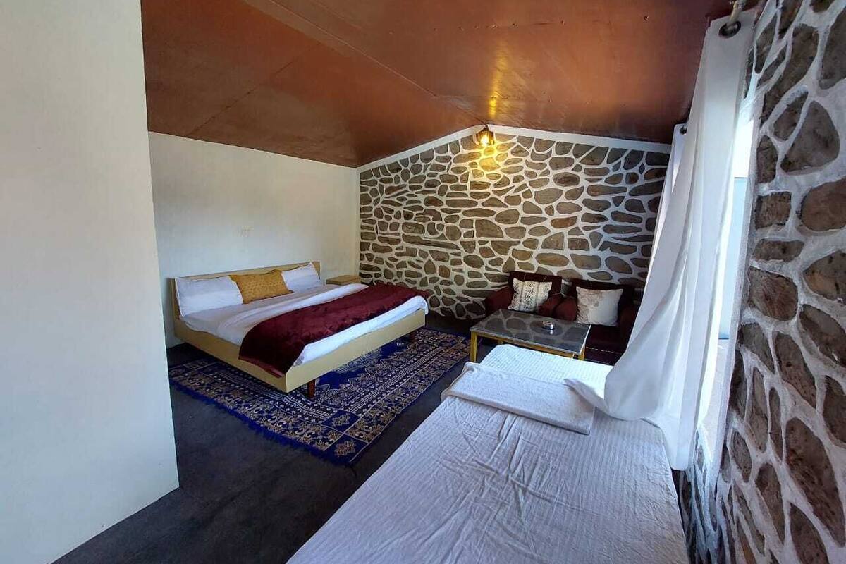 Ein Schlafzimmer mit Steinwand, einem Bett mit roter Decke, einem kleinen Tisch und einem Nachttisch.
