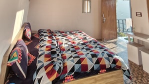 Ein Schlafzimmer mit Holzbalkendecke, einem Bett mit farbenfroher Steppdecke, einem kleinen Tisch und einem Fenster mit Blick.