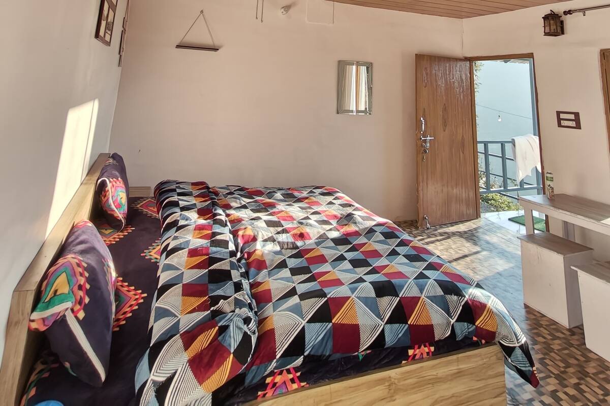 Ein Schlafzimmer mit Holzbalkendecke, einem Bett mit farbenfroher Steppdecke, einem kleinen Tisch und einem Fenster mit Blick.