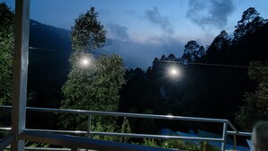 Ein Nachtblick vom Balkon mit Geländer, der eine gebirgige Landschaft mit Bäumen und wolkenlosem Himmel zeigt.
