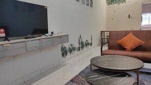 A modern room with a flat-screen TV, a sofa with an orange pillow, and a marble-patterned coffee table. - ForgetMeNot Pangkor Homestay 70 小蓝花民宿  4-bedroom villa with WiFi, AC (Pangkor)