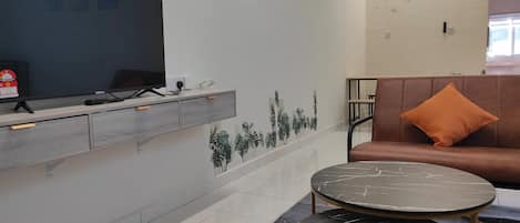 A modern room with a flat-screen TV, a sofa with an orange pillow, and a marble-patterned coffee table.