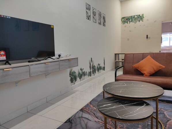 A modern room with a flat-screen TV, a sofa with an orange pillow, and a marble-patterned coffee table.