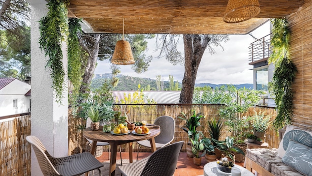 Une terrasse extérieure avec une table en bois, des chaises en osier et un coin salon agrémenté de coussins.