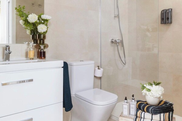 Un baño moderno con inodoro blanco, cabina de ducha de vidrio y tocador con espejo y artículos de aseo.