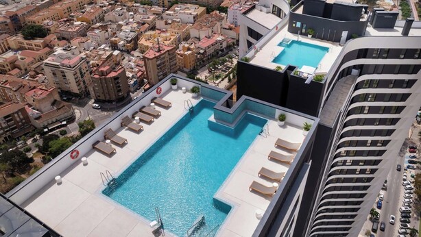 Una piscina en la azotea con tumbonas y un flotador salvavidas, rodeada de edificios urbanos.