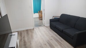 Une pièce avec un plancher en bois, un canapé noir, une chaise en bois et une petite table sur laquelle se trouve un cadre photo.