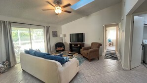 Una sala de estar con sofá, sillón, televisor y ventilador de techo.