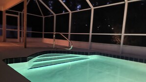 Una piscina con una escalera metálica y un cerramiento de vidrio.
